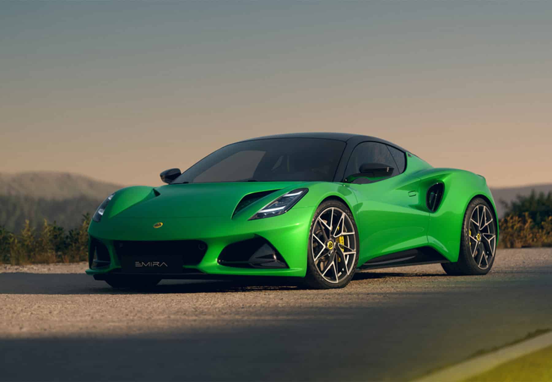 Grüner Lotus Emira Sportwagen auf Straße vor Berglandschaft bei Sonnenuntergang.
